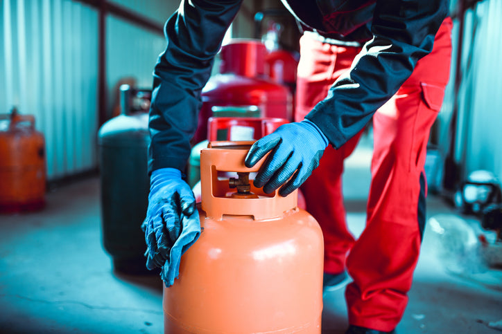 Eine Person in roter Hose putzt über eine orangene Gasflasche