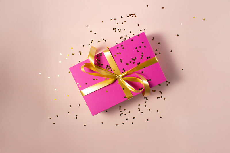Pinkes Geschenk mit goldenem Schleifenband und goldenem Konfetti auf rosafarbenem Hintergrund