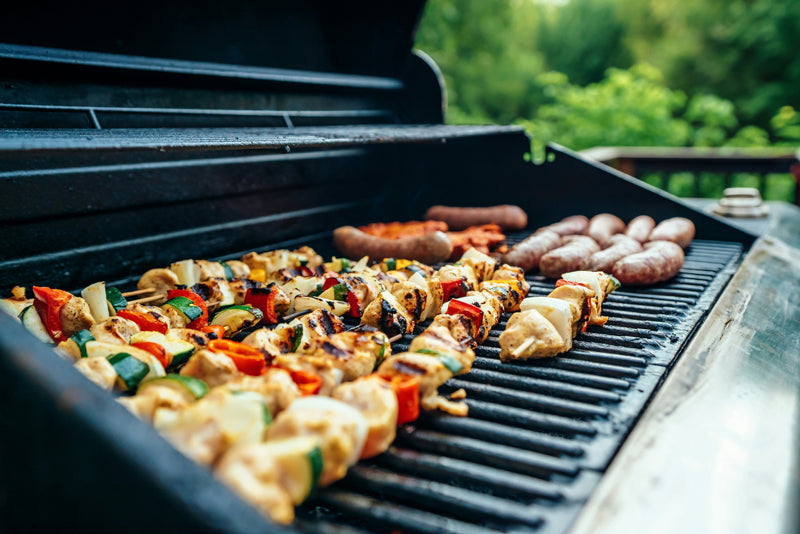 Grillrost von einem Gasgrill mit Gemüsespießen und Bratwurst