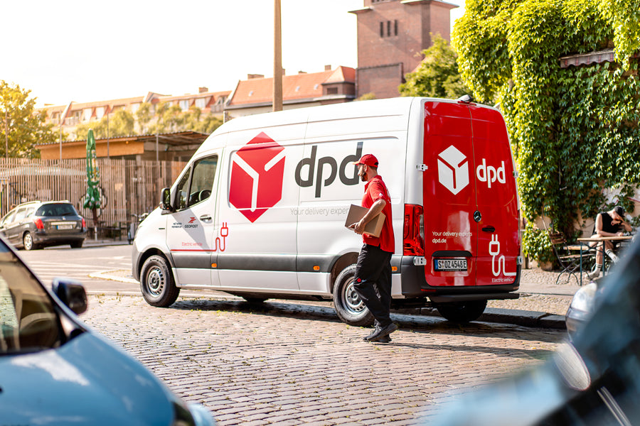 Ein DPD-Transporter steht auf der Straße, davor ein Paketbote mit einem Paket unterm Arm